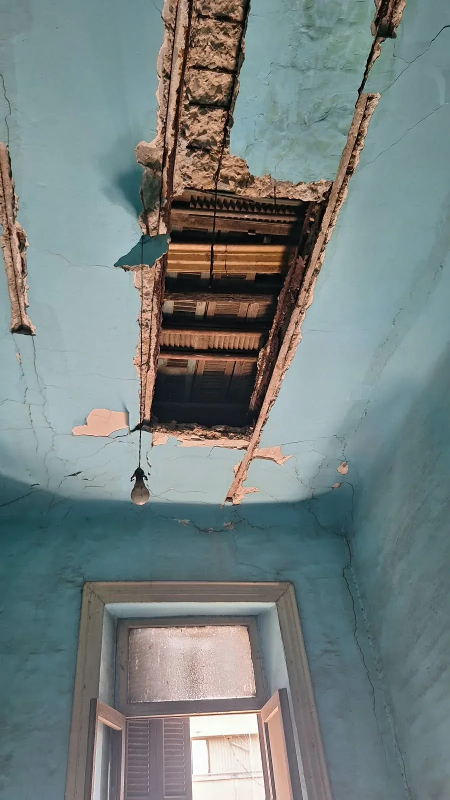 Old ceiling with cracked paint and exposed sections above a window opening